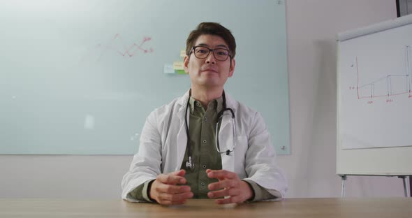 Portrait of asian doctor smiling and waving on video call looking at the camera alt