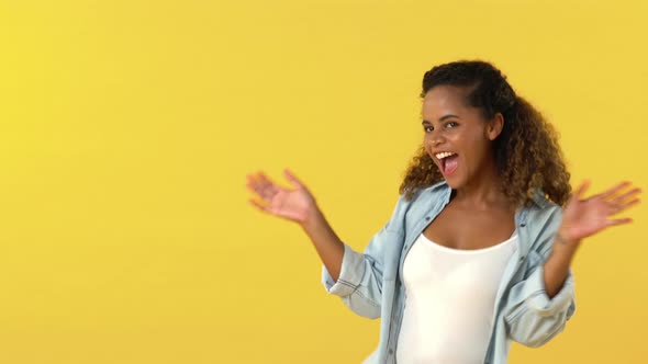 Happy young pretty African American woman smiling and dancing on yellow studio background