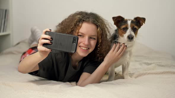 Beautifu Teenage Girl Ltake a Photo Selfie Bu Mobile Phone with Her Cute Dog in Cozy Bedroom