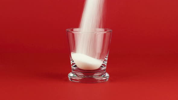 Pour Sugar in a Glass Shot with a Thick Bottom on a Red Contrasting Background alt