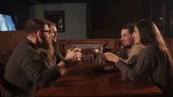 Two Pairs Are Sitting at Table in a Bar and Drinking Cocktails alt