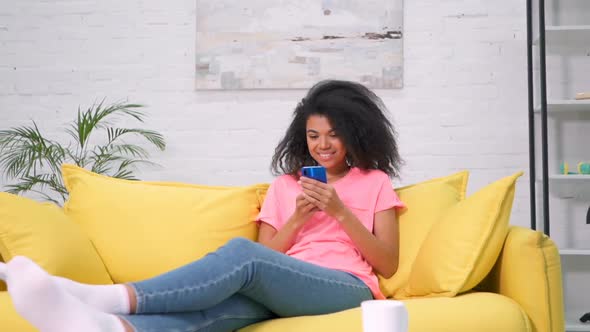 Smiling woman sitting on the sofa in the living room, Holding mobile