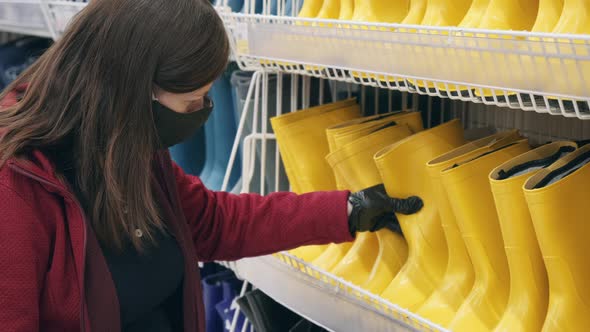 Caucasian Woman Wearing Mask and Gloves Against Virus Buys Rubber Boots in Shop