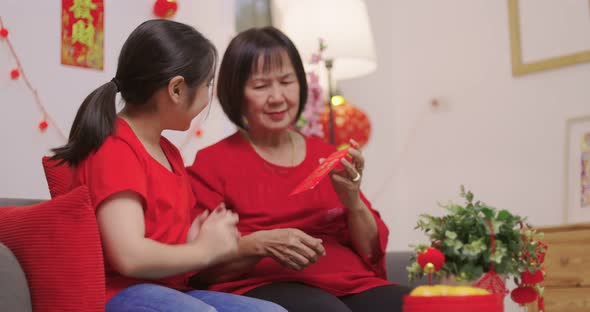 Happy Senior Asian Woman Giving Her Granddaughter A Lucky Red Envelope for Chinese New Year Gift. alt