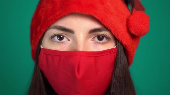 Portrait of Young Woman with Red Medical Face Mask and Santa Hat, Looking at Camera alt