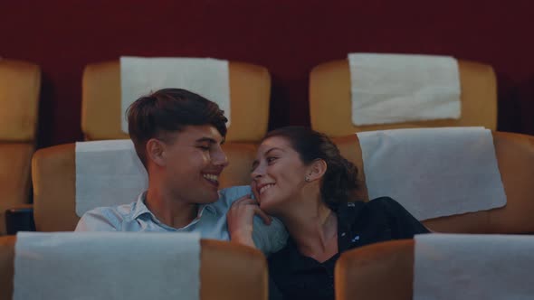 Attractive cheerful young caucasian couple laughing while watching film in movie theater. alt