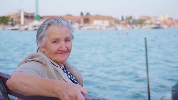 Elderly Woman Traveler Sits on Embankment of Chioggia alt