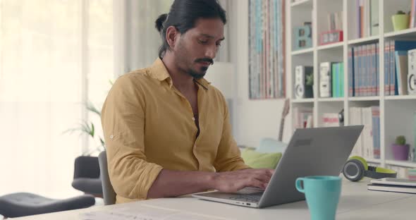 Indian man sitting at desk and typing with his laptop, he is working from home