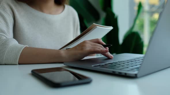 woman writing and working on laptop touchpad with mobile phone