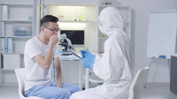 Doctor in Hazmat Suit Writing down Patients Symptoms alt