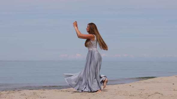Cute Young Woman in a Long Dress Dancing on The Beach 