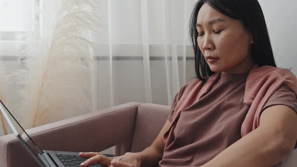 Asian Woman Using Computer in Armchair alt