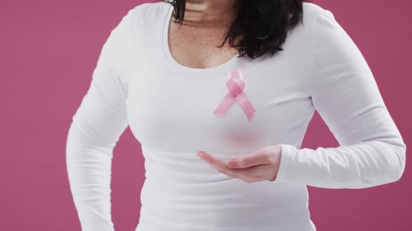 Mid section of woman with pink ribbon on her chest holding invisible object against pink background alt