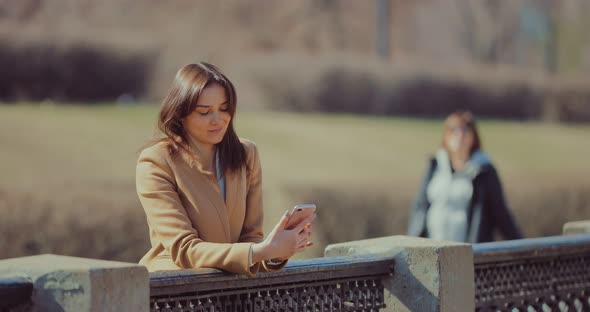 Young Beautiful Woman Stands at the Parapet and Dials SMS in the Phone alt