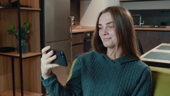 Smiling Relaxed Young Woman Hold Smartphone Watching Social Media Stories Video Siting on Sofa in alt