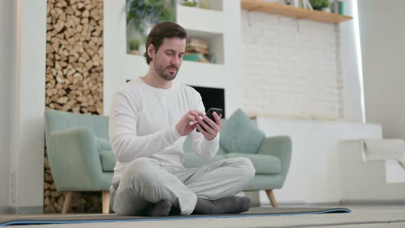 Young Man Using Smartphone on Yoga Mat at Home alt