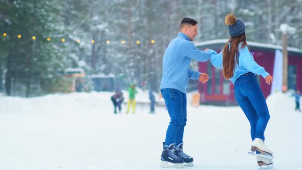Girl in Hat Skates Around Happy Guy on Outdoor Ice Rink