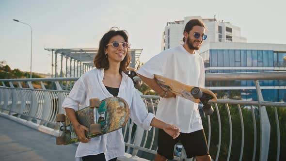 Young Couple in Love Walking with Skateboards on Bridge Slow Motion alt