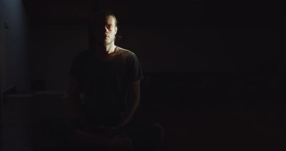 Portrait of Man Sitting in Lotus Asana Meditating Alone in Dark Room Black Background Copy Space
