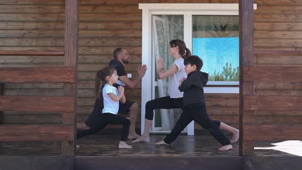 Family Does Yoga in the Warrior Pose on the Terrace Parents with Children Do Yoga on the Veranda at