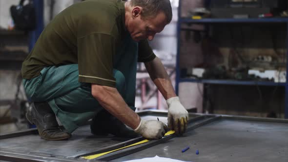 Locksmith Measures Tape Measure Length of Metal Bars and Makes Marks in Workshop alt