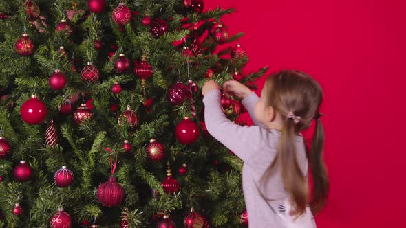 Little Cute Child Decorate Xmas Tree with Christmas Candy Cane on Red Background