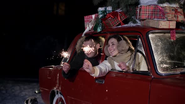 Happy Couple Sitting in Car and Holding Sparklers at Christmastime alt