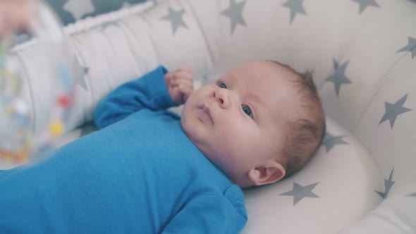 Mother Plays with Cute Kid in Blue Holding Rattle Over Crib alt