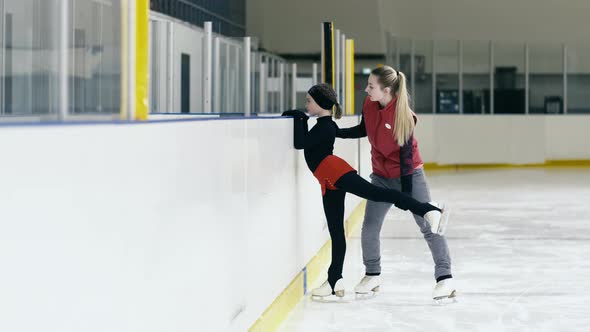 Figure skating coach showing right position of leg to girl on skate