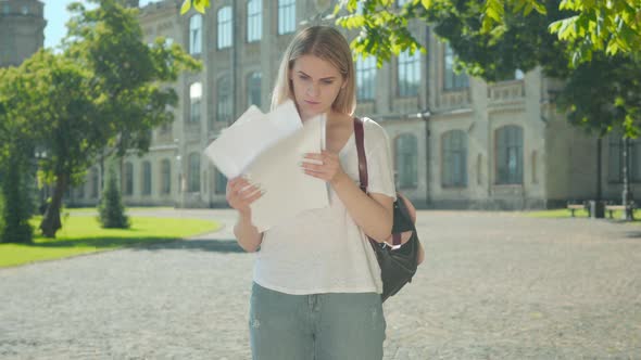 Joyful Happy Young Woman Checking Test Results, Throwing Papers Up and Spinning on University Yard alt