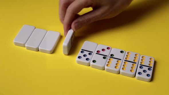 The hands of a young caucasian woman turn over dominoes in a row.