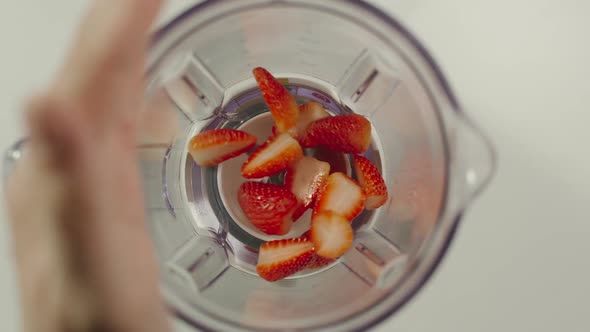 Pieces of strawberry fall into mixer from a hand