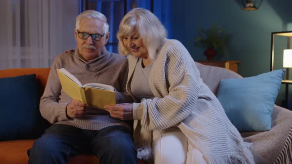 Senior Grandparents Couple Relaxing Reading Book Talking Enjoying Leisure Hobbies at Evening Home alt