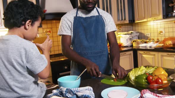 Father preparing salad while son drinking juice near