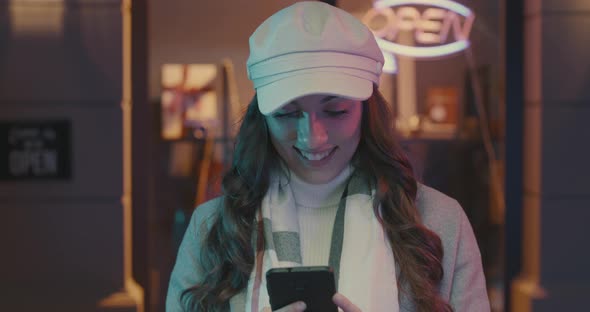 Happy young fashionable woman walking in the city street and connecting with her smartphone