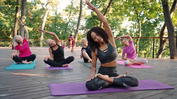 Happy Senior Women Practicing Yoga with Female Coach Sitting in Lotus Position on Mats and Repeating alt