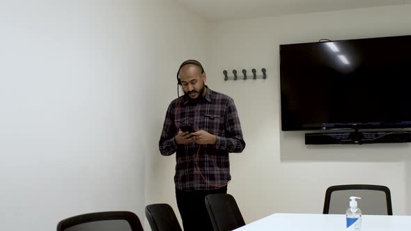 An Indian man pacing up and down a boardroom talking to a colleague on his mobile phone, the man foc alt