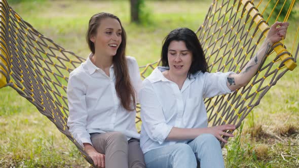 Two Young Caucasian Women Swinging Sitting in Hammock Talking in Slow Motion alt