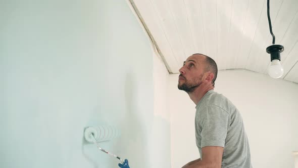 Caucasian Man Paints the Wall with a Roller Man Stands on a Stepladder Dad Makes Repairs in the Room