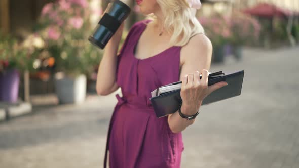 Closeup Business Papers and Books in Female Hand with Blurred Unrecognizable Adult Woman Drinking alt