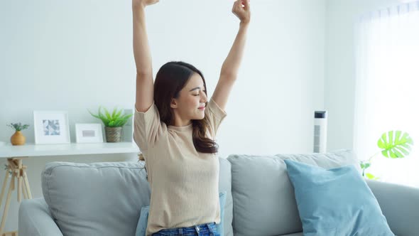Asian beautiful woman sit on sofa feeling happy and relax then stretched hands in living room. alt