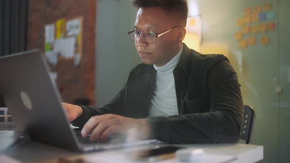 Close Up Portrait Of a Young Businessman Wearing Glasses Sitting in His Office Working Late At Night alt