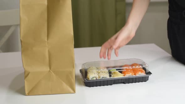 Food delivery concept: woman takes out delivered sushi boxes with japanese food. Take away food. alt