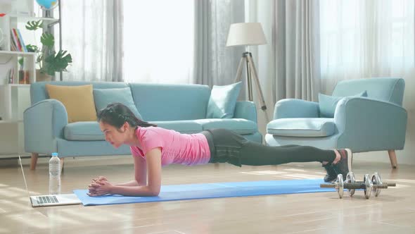 Asian Woman Doing Plank And Watching Online Tutorials On Laptop, Training In Living Room alt