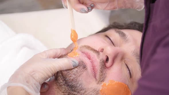 Concept of Cosmetology and Facial. A Woman Beautician Makes Face and Beard Modeling for a Man Waxing alt