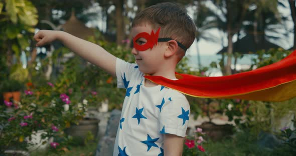 Cute Baby Boy in a Superhero Costume Dressed in a Red Cloak and a Hero Mask Waving Looking Into the alt