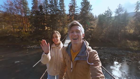 Slow Motion Happy Hikers Couple Walks Together on Wooden Suspension Bridge Hanged Over Mountain alt
