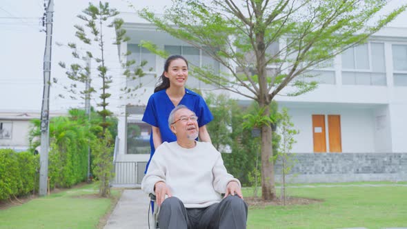 Asian caregiver nurse take care senior male sit on wheelchair outdoor at nursing home alt