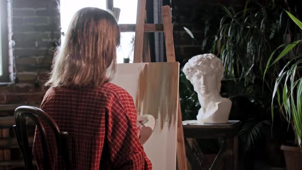 A Young Woman Artist in a Workshop Applying Base Colors on a Canvas with a Small Brush alt