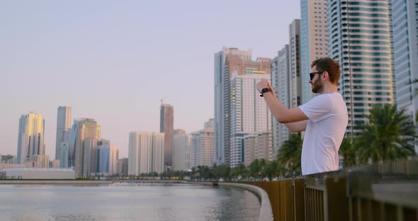 A Man in the Summer Standing on the Waterfront Photographed on a Smartphone Landscape of the City alt